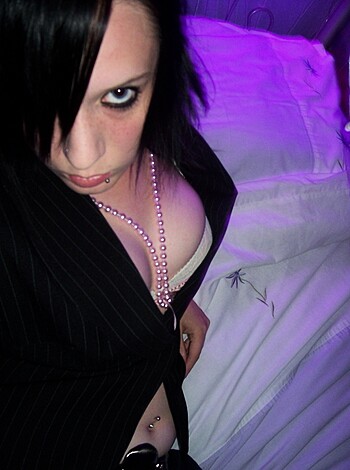 A busty broad lying on a bed with her tits hanging out of her bra and coat, rubbing her chest.