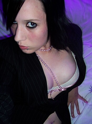 Here's the image of a hot babe with perfect tits layin' on a bed in purple lighting, wearin' a black top that shows off her bra and pearls while her nipples are poppin' out.