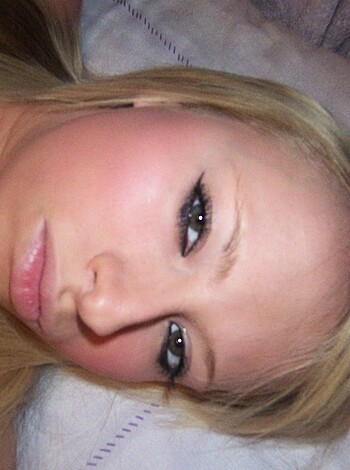 """
Close-up of a busty blonde chick with some makeup and an unnatural hair color, maybe even a wig. Her tits are all pushed up for the camera in her low-cut top, while her face looks like it's been smothered in foundation and lipstick. Maybe her hair is dyed red but who really gives a fuck when she's got those boobs to look at?
""" 
(27 words)