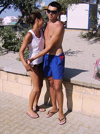 Here's the factual description of the image:
The dude is humping the chick on the shore with her thong showing, while their sandcastles are crumbling down and they're both blissfully ignoring it in a make-out sesh.