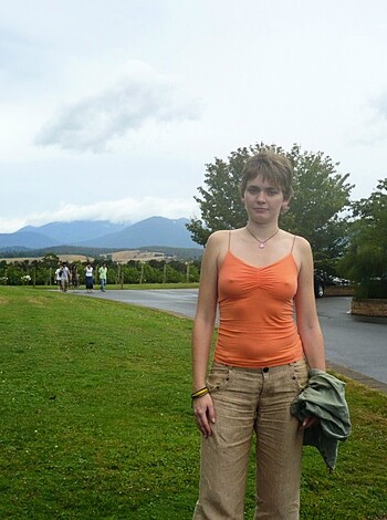 """
A fuckin' dude in some dumb-assed outfit stands beside a dirt trail in a shithole park while trees, bushes, and mountains serve as the backdrop to this bullshit scenario.
"""