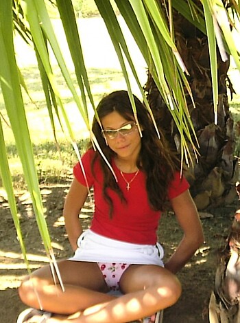 A blonde bimbo with a perfect ass sits beneath a palmy plant, taking a shit in the sand.