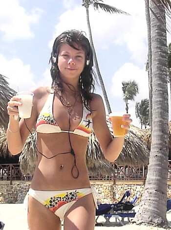 Busty blonde chick sipping fruity drink on a sunny beach while sporting a skimpy bikini.
