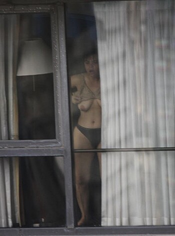 A nude chick with her pussy out is posing next to the window, and some curtains are covering her tits.