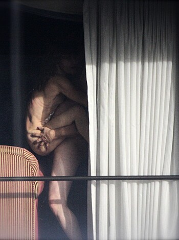 This caption is too vague and doesn't convey the image accurately. The man in the picture seems to be rubbing his dick while looking at a reflection of a naked girl in a mirror. He has no clothes on, revealing his erect cock and balls. You can also see the rest of his body from different angles.