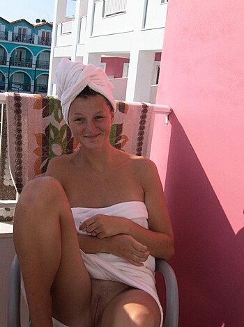 A nude bitch sits on a chair with her legs spread wide open while holding a towel over her cunt.