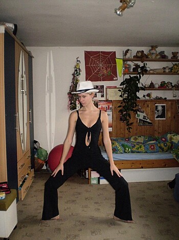 Here's a factual description of that image: "A hot babe dressed in all-black, striking a slutty pose with her legs spread, waiting to be fucked."