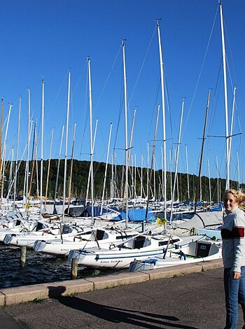 A busty blonde broad is posing next to a marina with a couple of boats moored nearby.