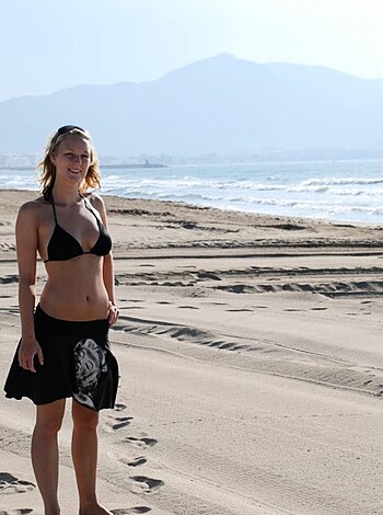 A naked babe in a hot swimsuit poses on the sandy shore.