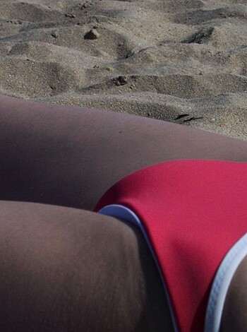 A busty broad wears a skimpy red one-piece while getting her pimply ass crack showed on the sandy shores of some godforsaken beach.