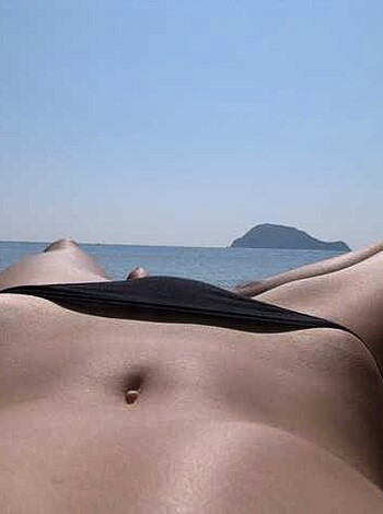 A naked chick sunbathing on a towel on the sandy shore, her ass hanging out for all to see.