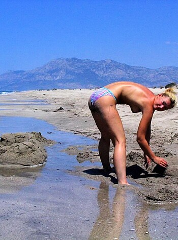 A nude chick on her hands and knees scooping up sand from the shore with her pussy exposed to the camera.