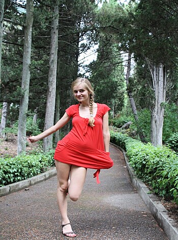 Red-dressed babe walks barefoot along dirt trail.