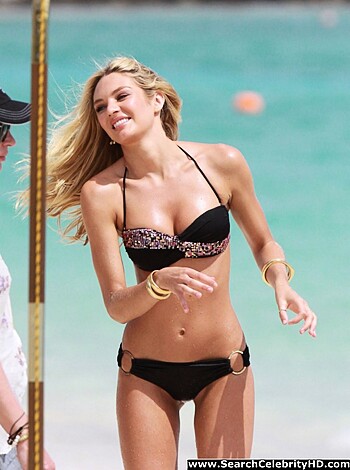 Busty blonde babe in a barely there bikini sunbathing on the sand, her tits jiggling as she moves while fucking guys on the shore watch.