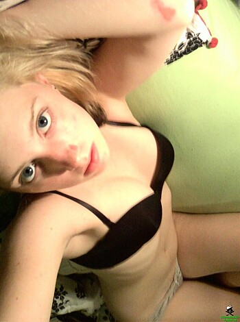 A chick with black bra and thong underwear is seated on a bed, spreading her legs while posing for the camera.