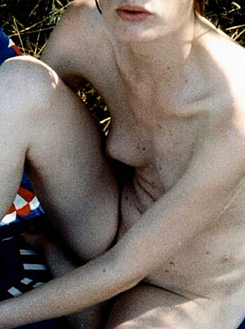 "A topless chick with tits and ass laid out on the grass, smiling for the camera."
