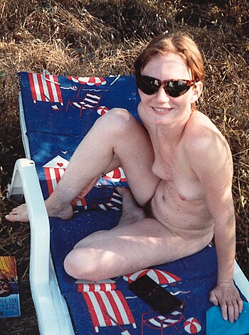 A topless chick sits on a beach chair, her boobs hanging out.