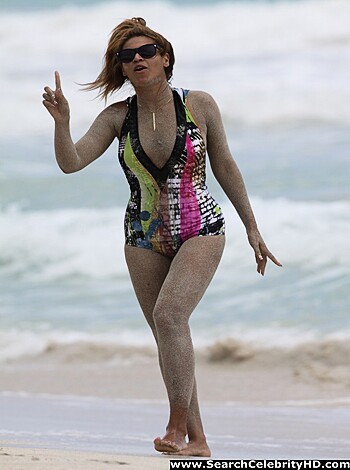A chick in a bikini struts her stuff along the shore while soaking up some sunshine.