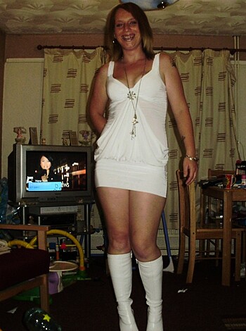 Here's the factual description of the image. The woman is sporting a tight-fitting, pristine white dress that hugs her body, emphasizing her curves. She's got black leather boots on with stiletto heels that accentuate her long legs and sexy figure.