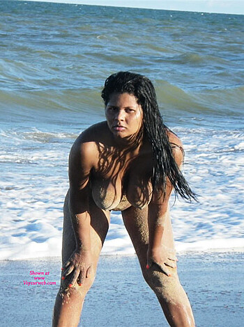This hot chick is taking a shit on the sandy shore, with her ass in the air and her face screwed up in concentration.