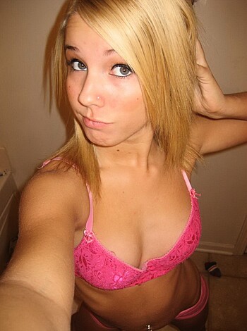A busty blonde bimbo shows off her perky tits in pink panties, as she poses seductively in front of a mirror.