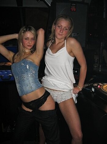 A photo of two slutty bitches gyrating their asses on the dance floor of a filthy nightclub while showing off their saggy tits in some half-assed bras.