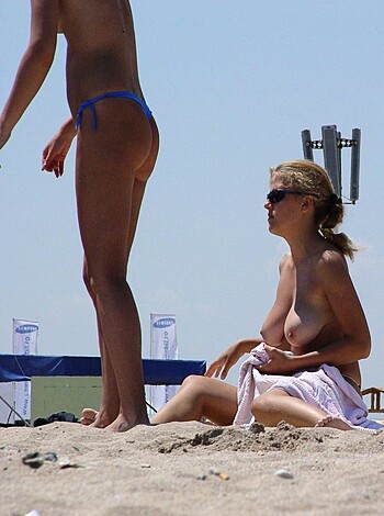 A couple of tits on display while laying on the shore with one chick sitting and the other standing, showing off her goods.