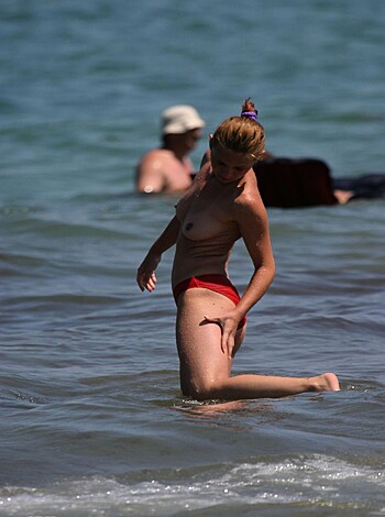A naked broad in a red string bikini dips her dunky bits into the surf, while fondling herself through her skimpy swimwear.