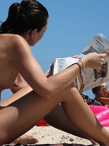 Here's the fucking caption: A busty blonde chick is lounging on a sunny shore, casually perusing some news while her nipples are fully exposed and she's flaunting her tits to everyone around.