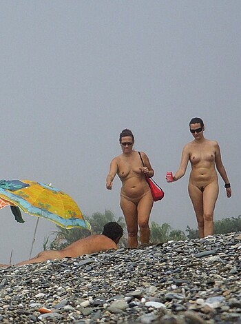 Here are some facts about this image: Two topless bitches strolling down the fucking shoreline, with their big tits hanging out for all to see.
