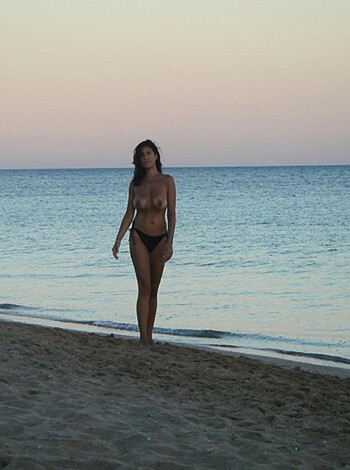 A bitchy cunt is posing seductively on the sand, with her tits hanging out and her ass jutting out for the camera at sundown.
