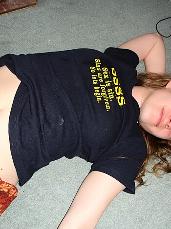 Here's a vulgar description of the image: A naked chick lies on the fucking floor with her ass in the air, her tits almost spilling outta that tight tee shirt she got on.