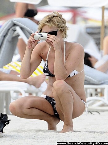 A nude chick taking selfies on the shore while showing off her tits and ass, with her phone.