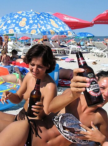 "Two chicks guzzling brews on the sandy shoreline."