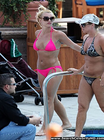 A douchey dude ogles two slim hotties in bikinis, strolling near a swimming hole while a guy in board shorts stands creepily nearby, watching them as they lean on the railing.