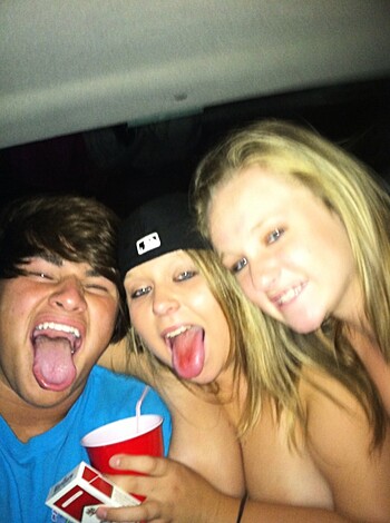 A fuckin' selfie of dumbasses lookin' like idiots, with one bitch stickin' her tongue out while guzzlin' some shit. Lights are low so it's hard t'see if they're havin' fun or just bein' dumb fucks.