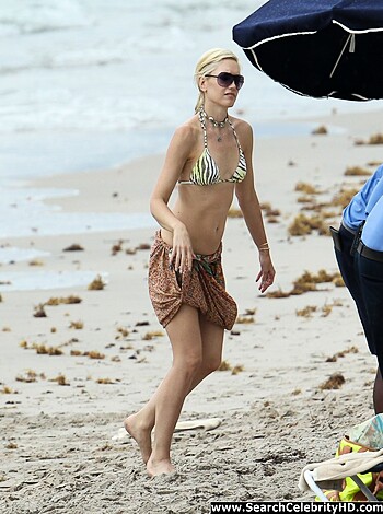 A tits-out blonde strolls down a sandy shoreline with her perky melons bouncing and swaying with each step she takes, her glistening pink nipples poking out through the thin fabric of her skimpy swimsuit.