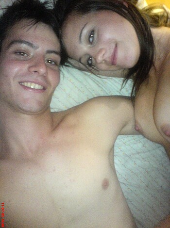 The photograph captures two hot chicks lying in bed together, with their pussies inches apart, grinning from ear to ear as they lock eyes.