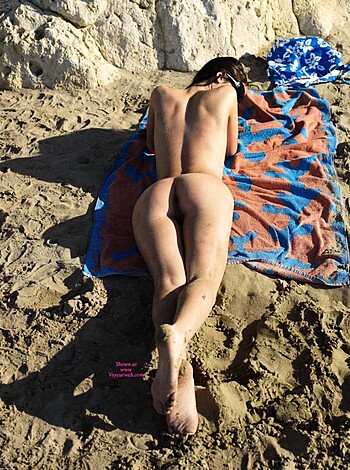 A naked dude is chilling on a fucking hot beach, soaking up some rays.