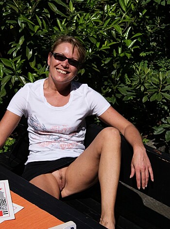 Vulgar description of the image: A fucking hot chick in a tight white tee and shades is enjoying some sweet ass time on a bench with her legs crossed, looking all sexy and shit while sporting a big grin.