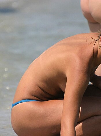 Fucking hot babe in her skimpy blue bikini panties squatting down on the sandy beach with her ass up while staring at something that seems to be really interesting.