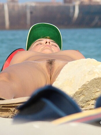 This dude's got no shirt on and he's chillin' on the sand, gazing up at the clouds.
