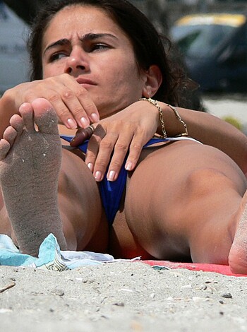 A bikini-clad chick's feet on the sandy shore, with her toes splayed out and her pinkies touching in a seductive manner.