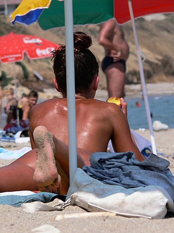 Here's the vulgar description of the image: The chick is lying on a beach towel, showing off her panty line in some skimpy bikini bottoms, soaking up some sun while sporting a sweet tan.