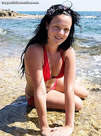 The chick in the tight red bikini is sitting on some rocks by the sea with her legs spread wide open and she's staring right at the fucking camera.