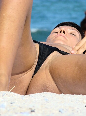A naked chick lying on the sand with her coochie exposed.