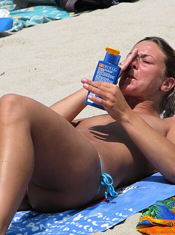 "Check out this hot chick on the beach, dousing her body in suntan lotion while sitting on a beach towel. In case you were wondering, she's wearing nothing but sandals - fuckin' smokin' ass bitch!"