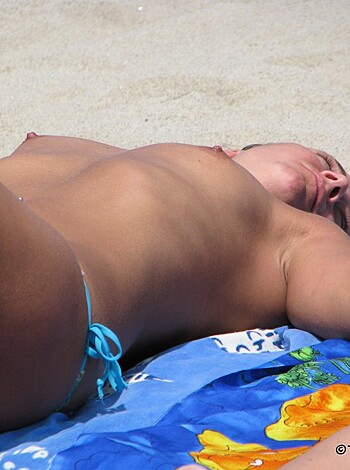 This picture depicts a hot babe who is laying flat on her back with her boobs fully exposed while enjoying the warmth of the sun's rays on her naked tits.