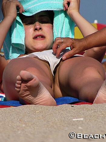 A chick spreads sunscreen on some dude's gams.