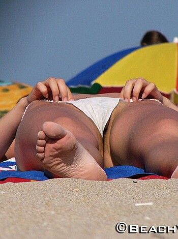 A sun-kissed pair of toes and ankles with some sand stuck between them, belonging to someone enjoying the beach scene.